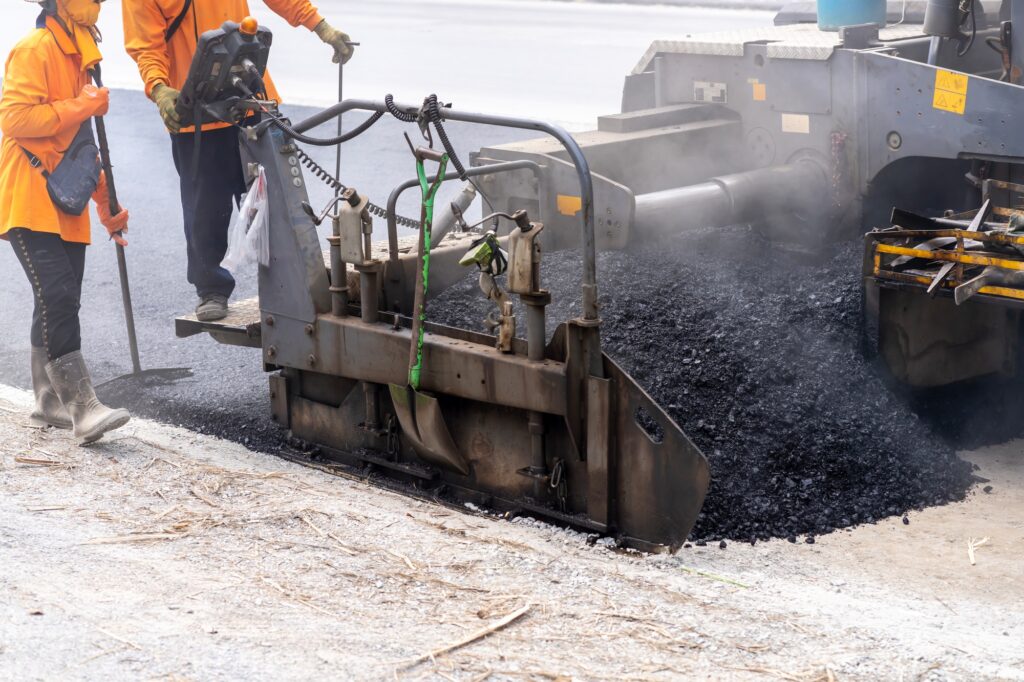 Machines are pouring asphalt to build roads for cars.